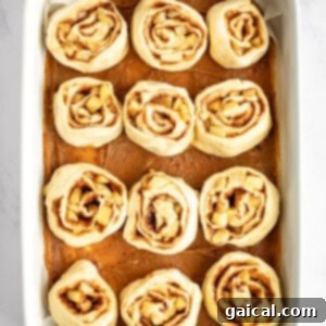 Gooey Cinnamon Apple Rolls 14 A white baking dish filled with twelve unbaked cinnamon rolls evenly spaced, ready for baking, on a white marble surface.