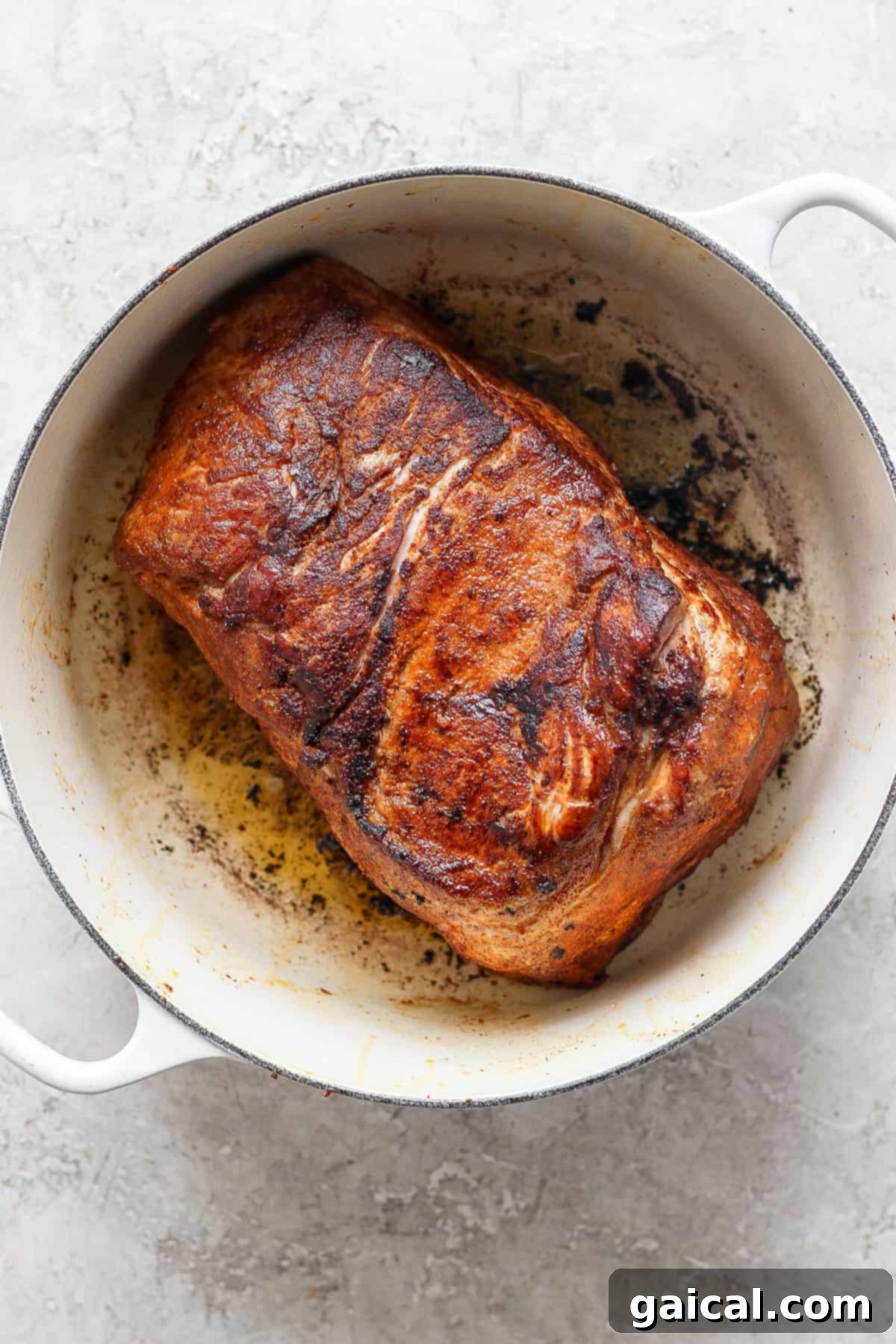 A cooked, browned piece of meat in a white pot, showing seared and crispy edges.