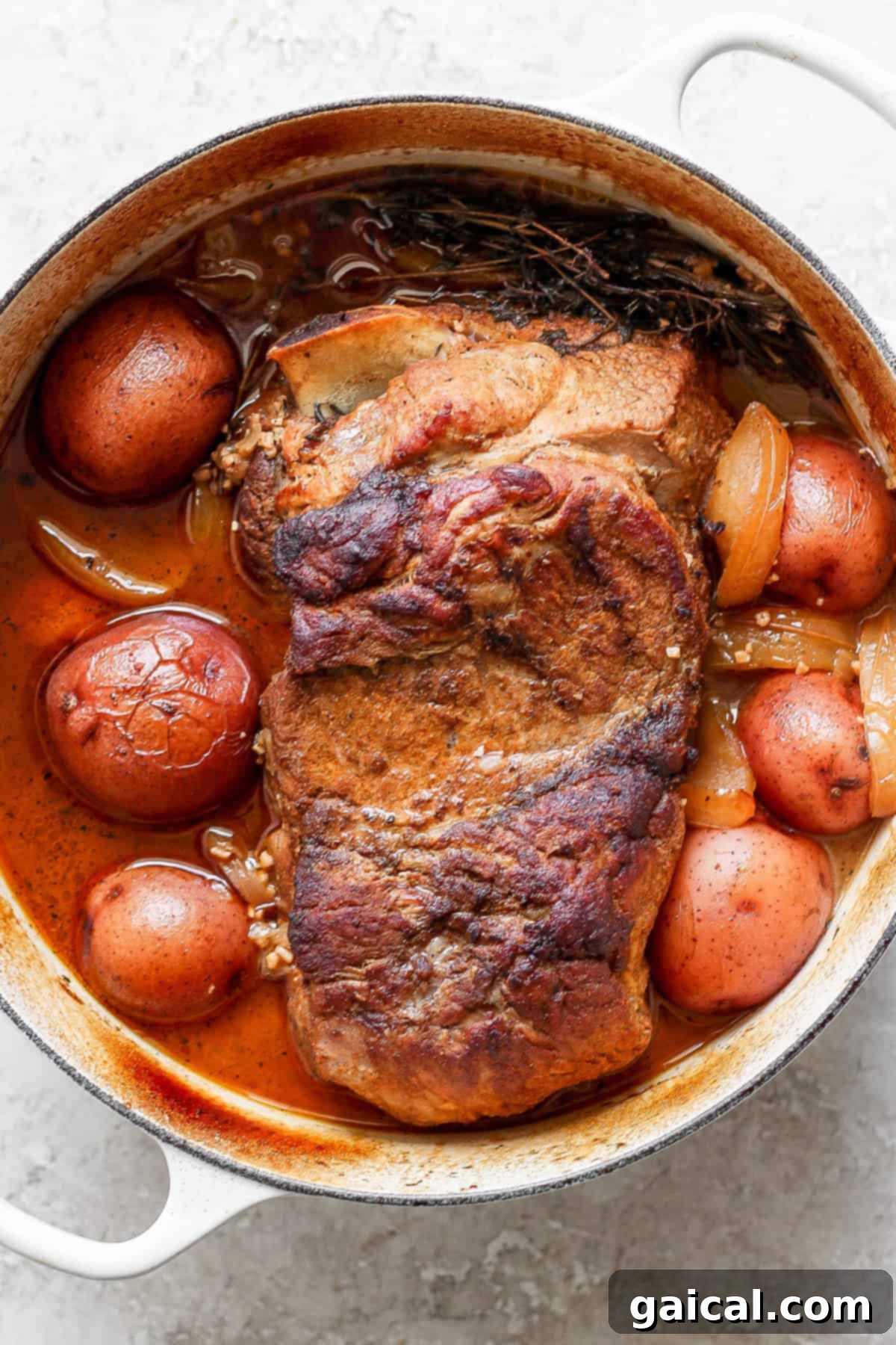 A cooked pot roast with potatoes and onions in a white enameled cast iron pot.