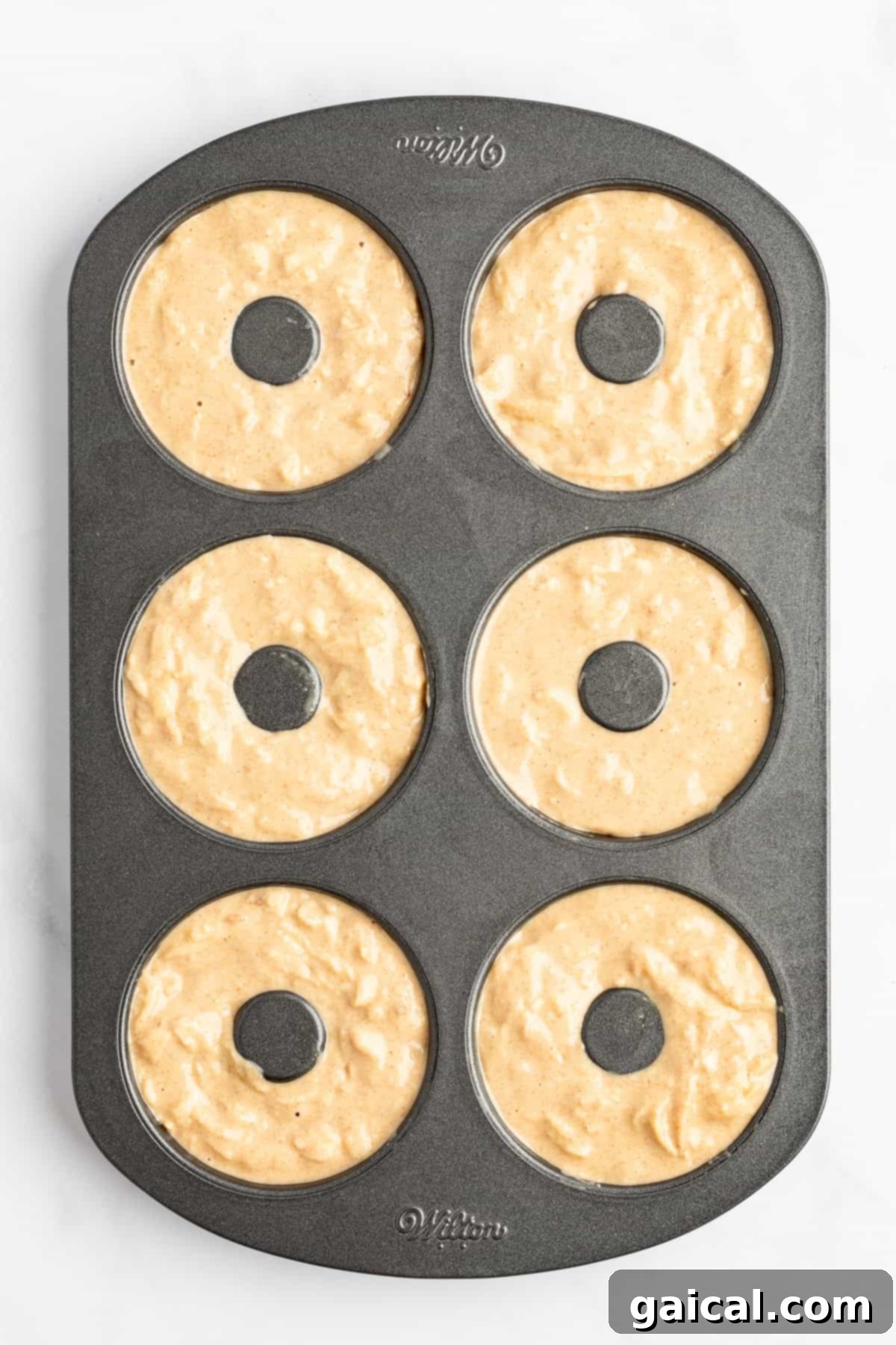 Spiced Orchard Doughnuts 5 A six-cavity donut baking pan filled with unbaked donut batter, piped perfectly into each mold, ready to be placed in the oven.