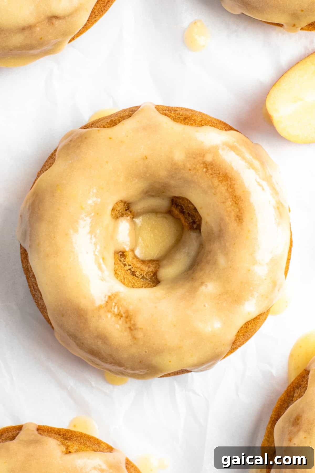 Spiced Orchard Doughnuts 7 Close-up of a perfectly glazed apple cider donut with a smooth, shiny brown butter coating, resting on a white surface. The texture of the baked donut is visible through the center hole.