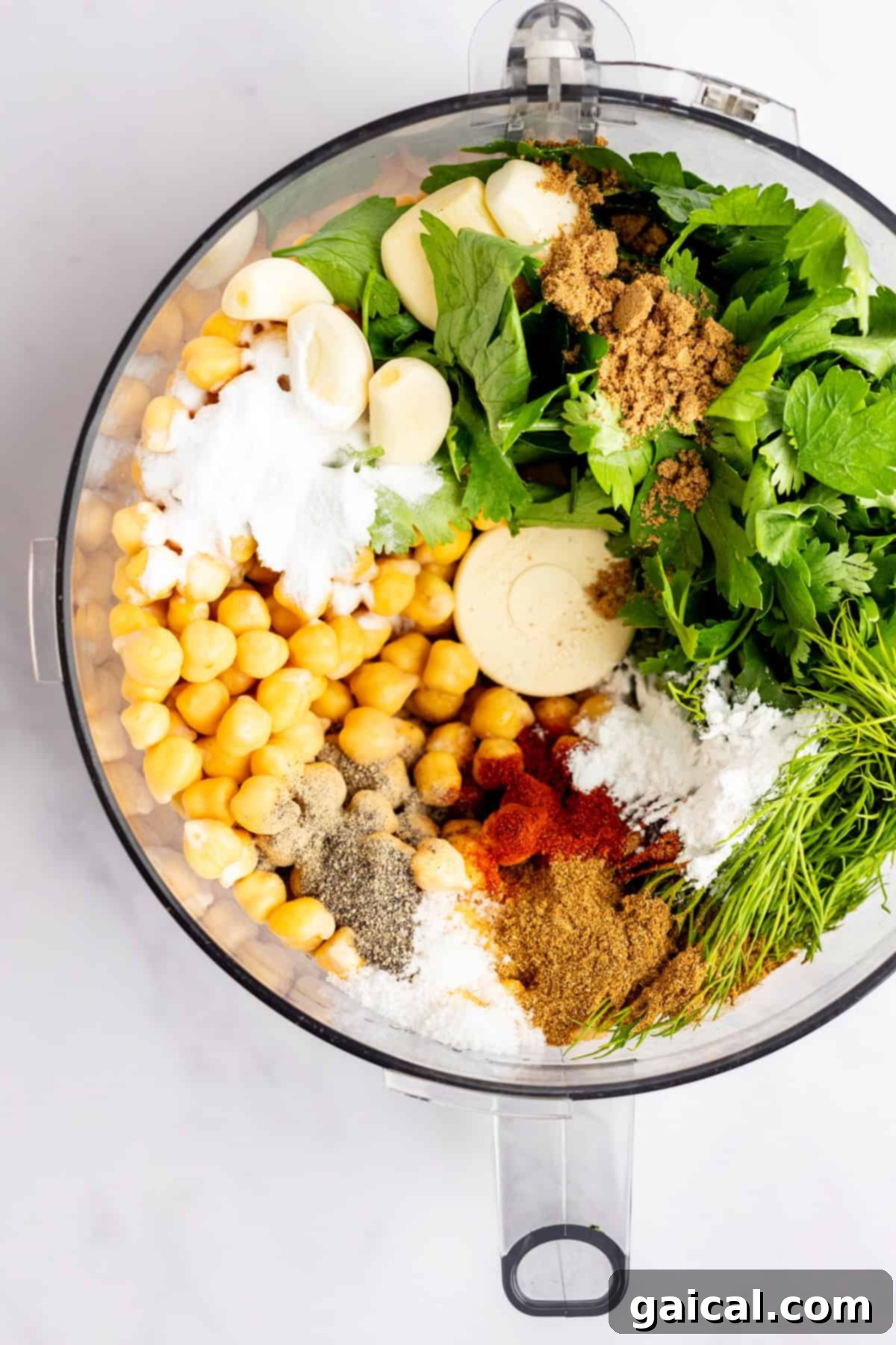 Food processor bowl filled with chickpeas, garlic, herbs, spices, and other falafel ingredients, viewed from above.