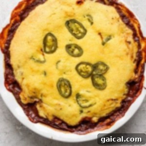 Effortless Chili Pot Bake 10 A baked dish in a round white pan, topped with cornbread and sliced jalapenos, with some edges browned and crispy.