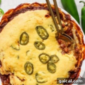 A dish of chili pot pie, with a golden cornbread crust, served in a round white pie dish, ready to be enjoyed.