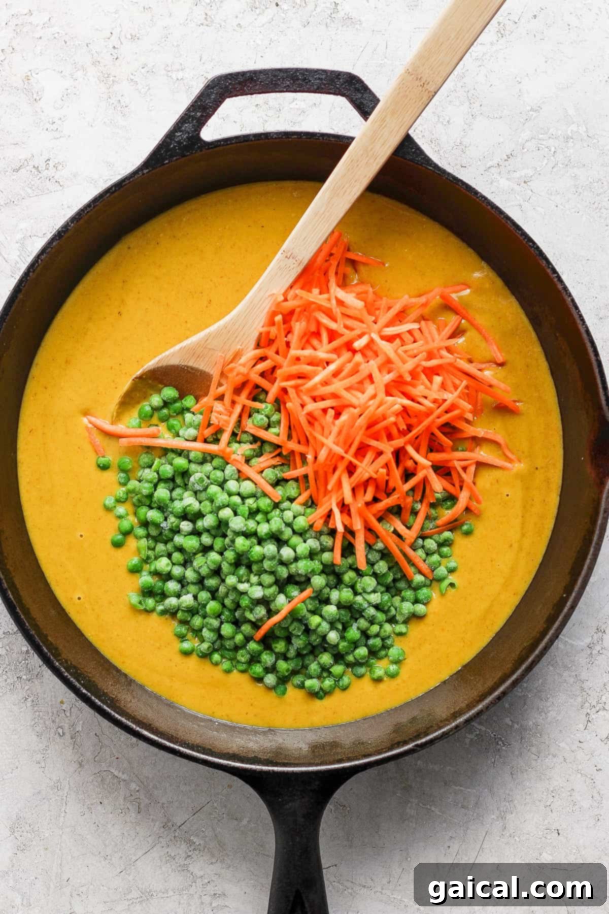 A cast iron skillet containing creamy soup garnished with a spoonful of green peas and a scattering of grated carrots on a light-colored surface.