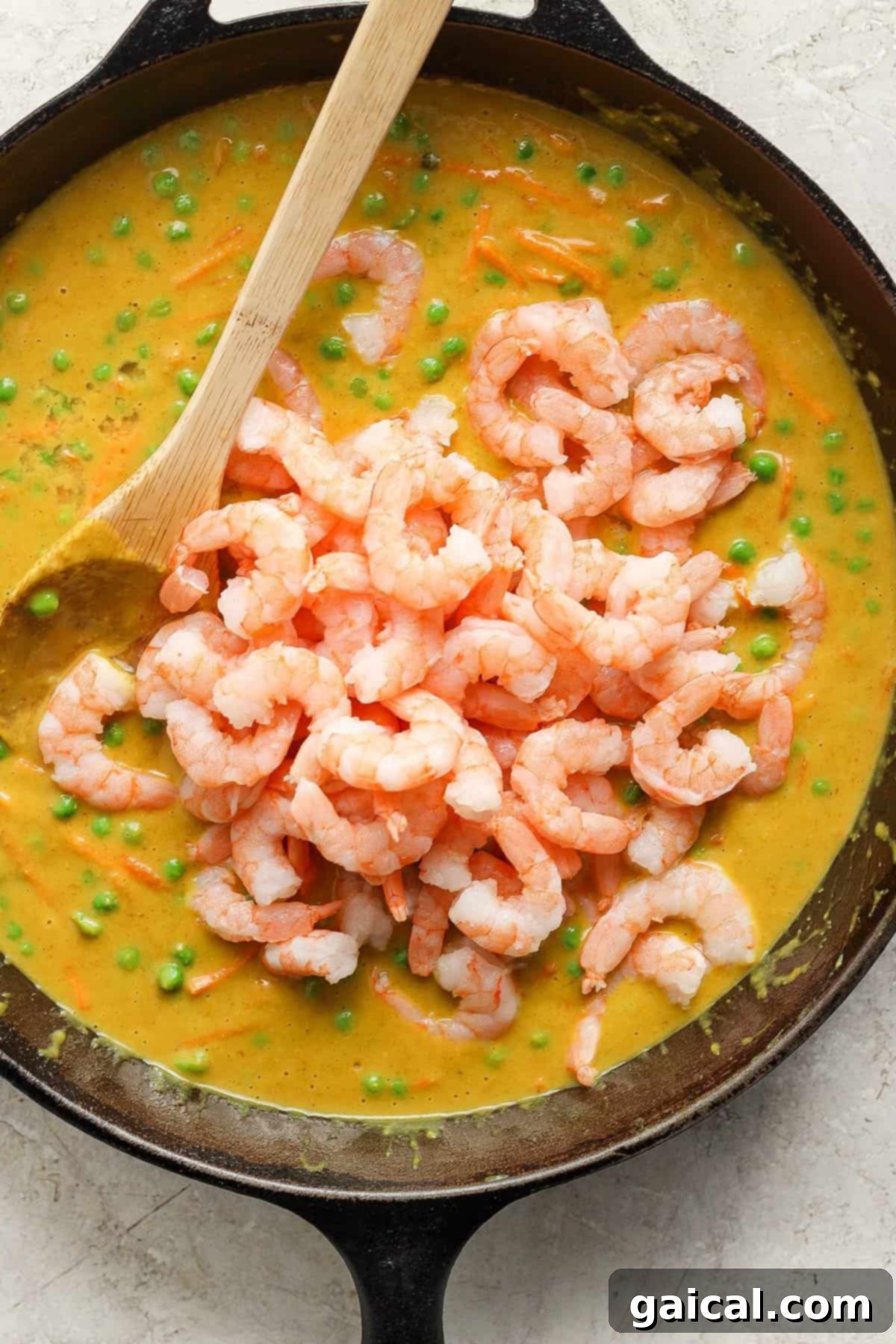 A skillet filled with a creamy pea soup topped with a mound of cooked shrimp, with a wooden spoon resting inside the pan.