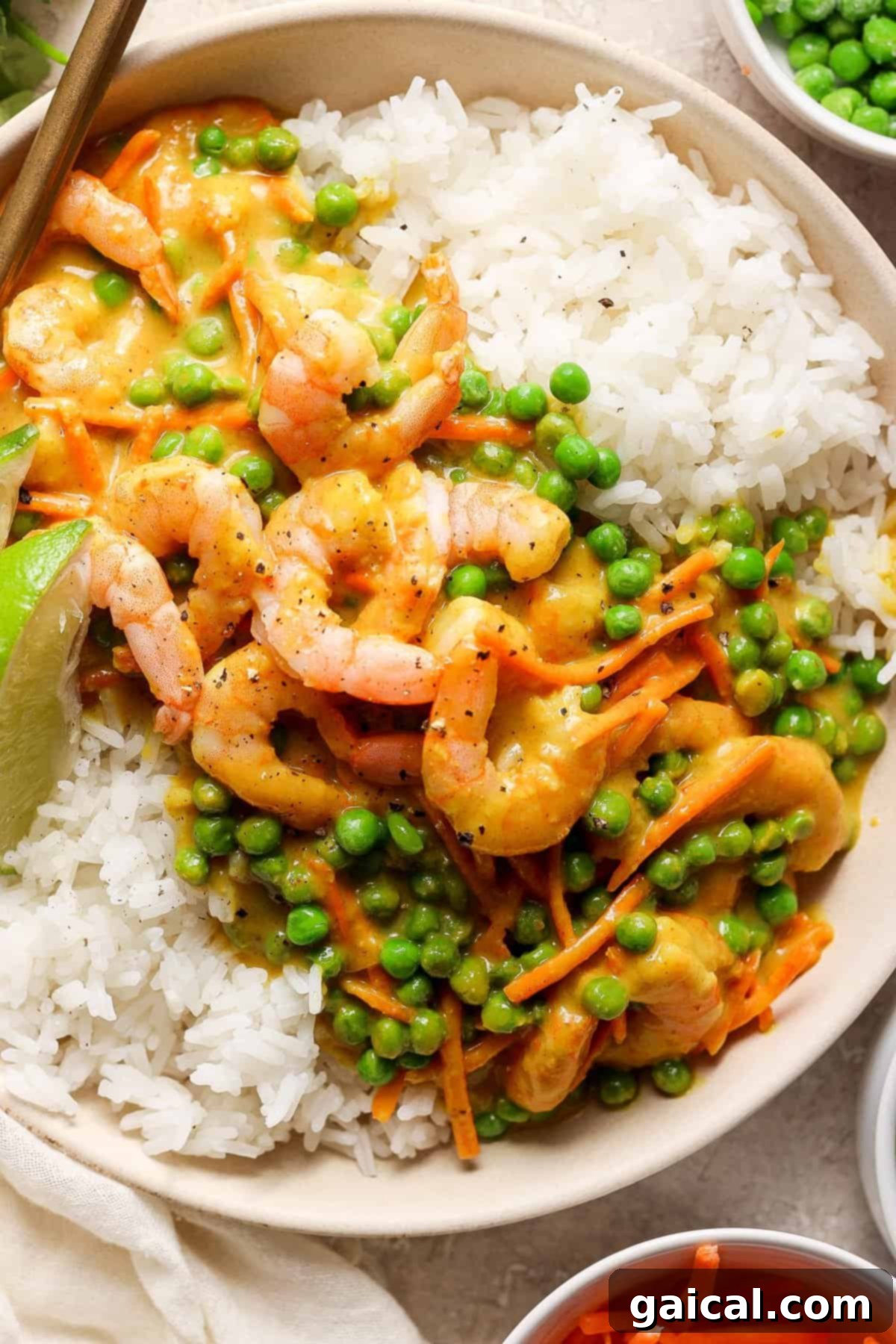 A bowl of white rice topped with shrimp and green peas in a creamy sauce, garnished with a lime wedge.