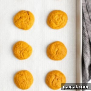 Eight freshly baked cookies on a parchment-lined baking sheet with a gray cloth visible on the right side.