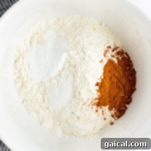 A white bowl containing flour, cinnamon, and baking powder, with a striped cloth partially visible in the background.