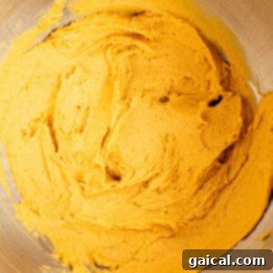 A stainless steel mixing bowl containing smooth, thick orange batter.