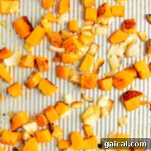Diced butternut squash and chopped onions spread out and roasted on a baking sheet.