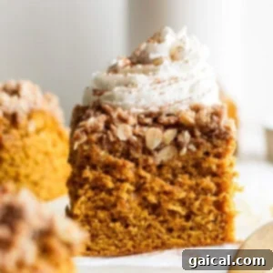 A slice of pumpkin crumb cake topped with whipped cream and a sprinkle of cinnamon, placed on a white surface.