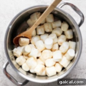 A pot filled with large marshmallows and a wooden spoon placed on a textured surface.