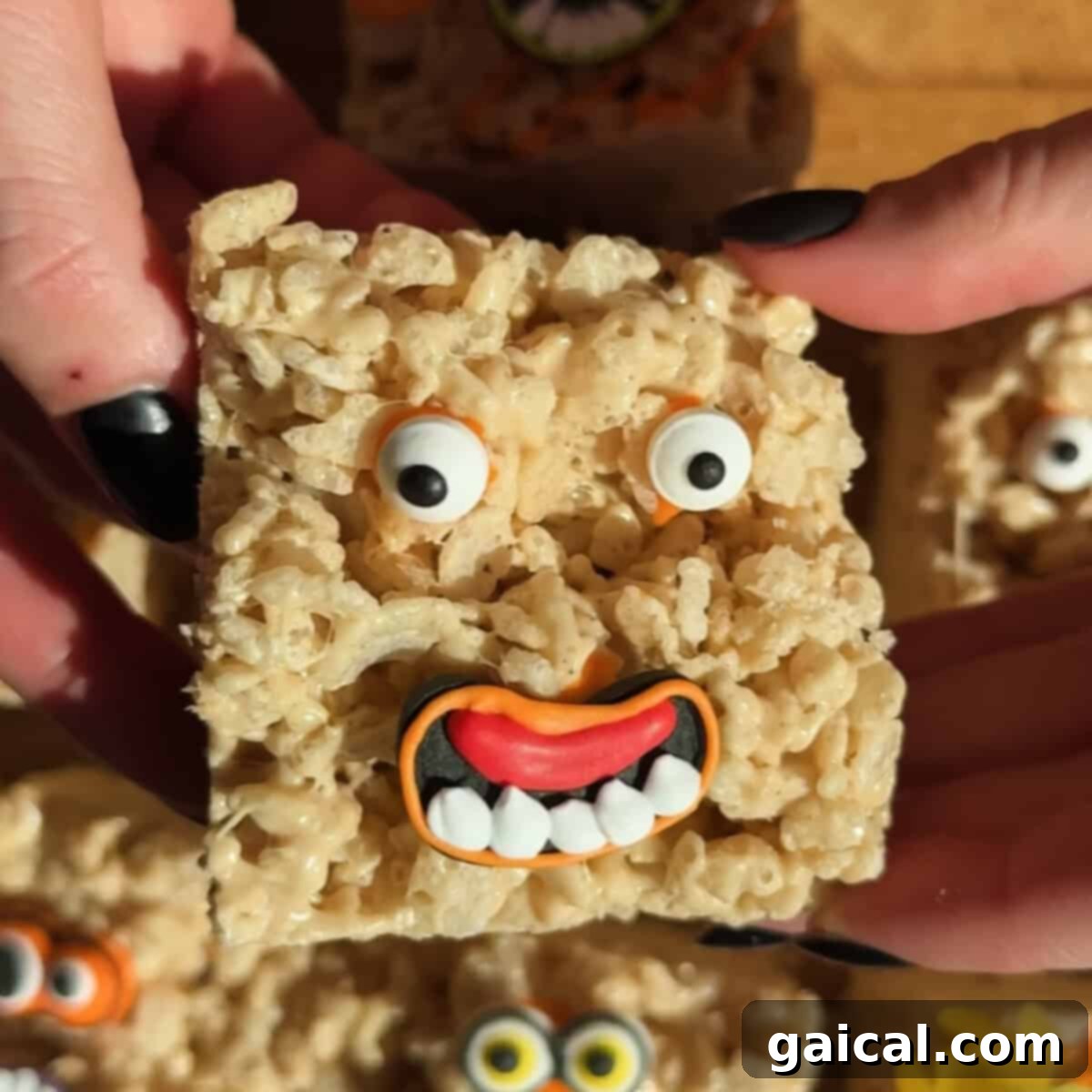 Aromatic Chai & Nutty Brown Butter Crispy Treats 5 A Rice Krispies treat decorated with candy eyes and a mouth, resembling a goofy face, is held between two hands with black-painted nails.