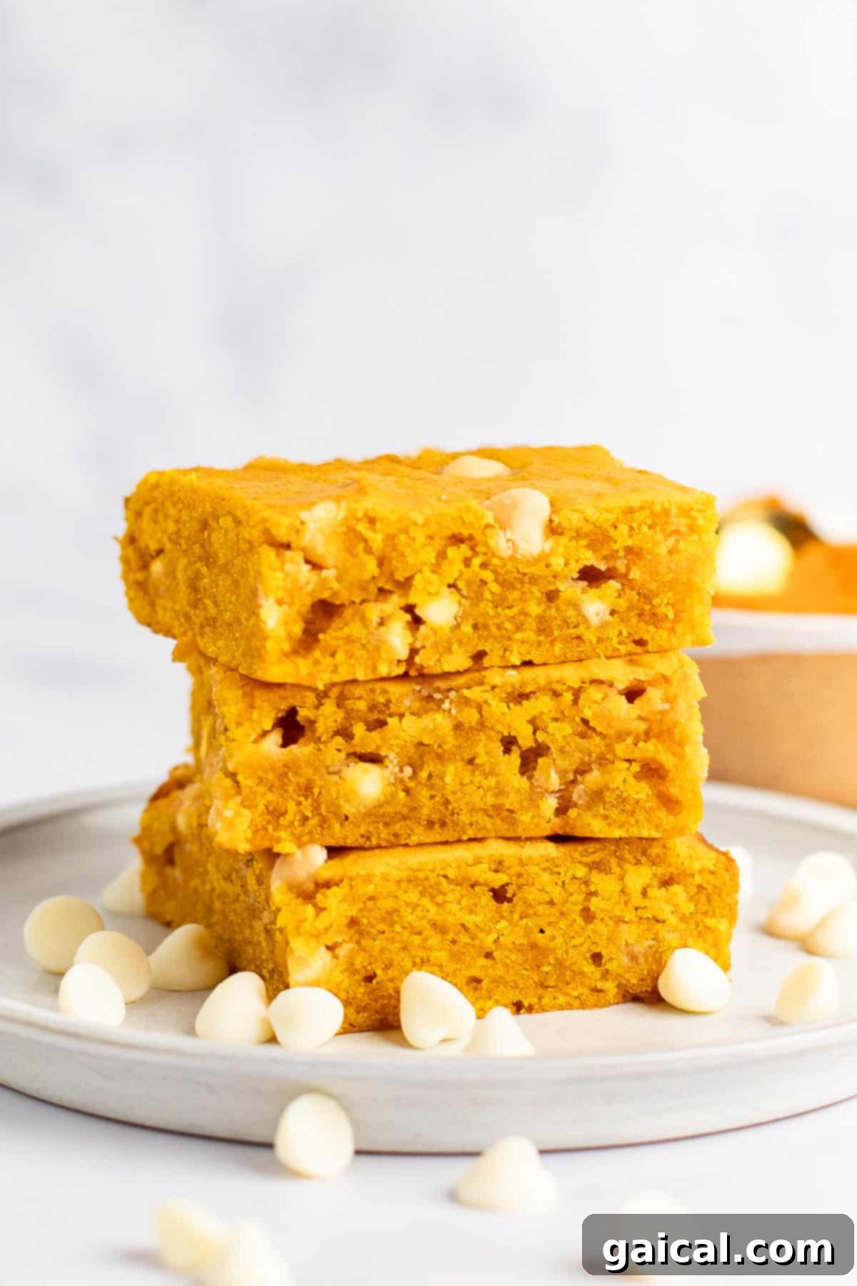 Warm Spiced Pumpkin Blondies 2 Three slices of golden yellow pumpkin blondies stacked on a plate, surrounded by white chocolate chips.