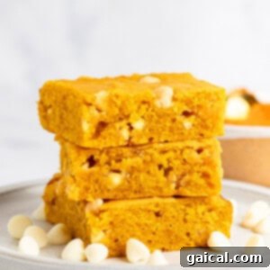 Warm Spiced Pumpkin Blondies 11 Three slices of golden yellow pumpkin blondies stacked on a plate, surrounded by white chocolate chips.