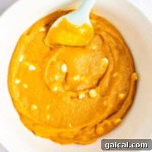 Warm Spiced Pumpkin Blondies 9 A bowl containing orange cake batter with white chocolate chips mixed in and a light blue plastic spatula.