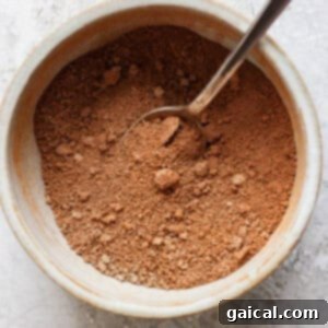 A spoon in a ceramic bowl filled with brown powder, set on a textured surface.