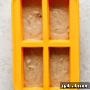 A yellow four-section silicone mold is filled with light brown batter on a light gray textured surface.