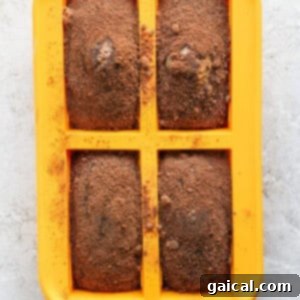 A yellow silicone baking mold with four rectangular cavities, each filled with a brown baked mixture dusted with a light coating of cocoa powder.