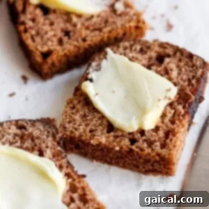 Slices of brown bread topped with thin pats of butter are placed on parchment paper next to a butter knife.