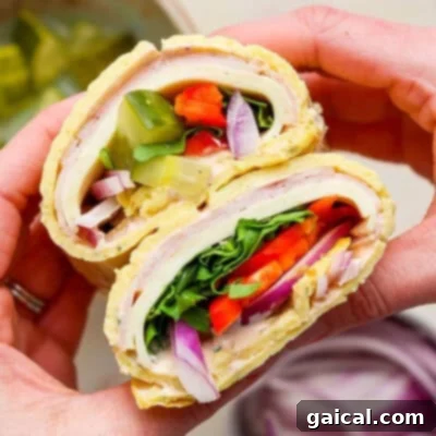 Hands holding a delicious cottage cheese wrap filled with turkey, lettuce, tomato, pickles, red onion, and spinach.