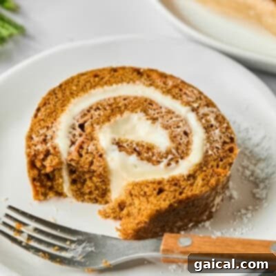 A slice of pumpkin roll with cream cheese filling on a white plate, partially eaten, with a fork beside it.