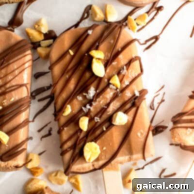 Chocolate-coated ice cream bar sprinkled with nuts and drizzled chocolate on parchment paper.