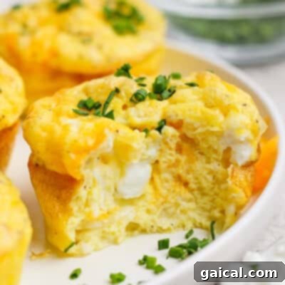 A baked egg muffin with a bite taken out, showing a fluffy texture and cheese inside, topped with chopped green onions on a white plate.