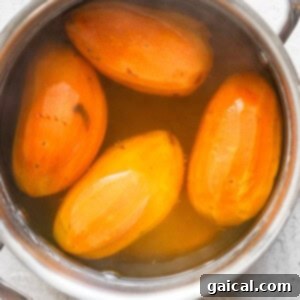 Four peeled sweet potatoes boiling in a stainless steel pot filled with water.