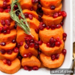 Sliced sweet potatoes topped with cranberries and garnished with a sprig of rosemary, served in a white dish.