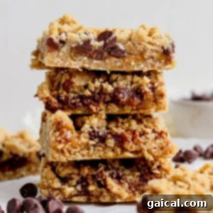A stack of four delicious chocolate chip oatmeal bars with a delightful crumbly texture, neatly presented on a pristine white surface, surrounded by a few scattered chocolate chips for visual appeal.