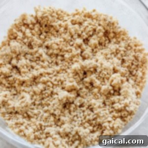 A transparent glass bowl containing a perfectly mixed, crumbly oat and butter mixture, ideal for a streusel or pie topping, resting on a clean, light-colored kitchen countertop.