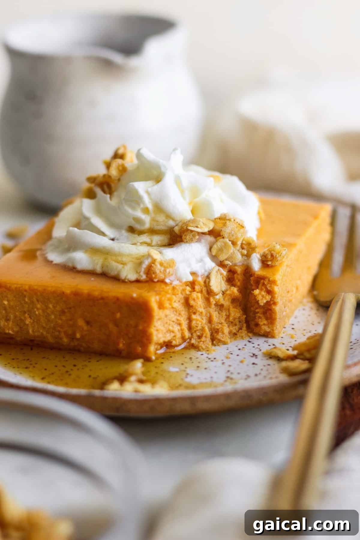 A slice of pumpkin cheesecake topped with whipped cream, granola, and drizzled with syrup, on a plate with a fork.