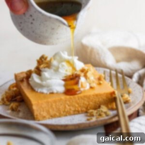 A hand pours syrup from a small jug onto a slice of cheesecake topped with whipped cream and granola. A fork and a napkin lie beside the plate.
