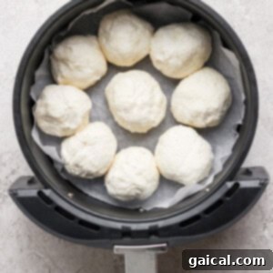 An air fryer basket lined with parchment paper holds eight uncooked dough balls in a circular arrangement.