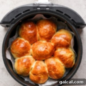 Golden brown homemade rolls arranged in a circular pattern inside an air fryer basket on a gray surface.