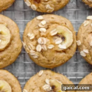 Freshly baked banana oat muffins cooling on a wire rack, topped with banana slices and oats, steam gently rising.