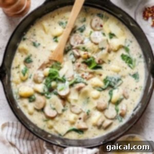 A skillet containing creamy gnocchi with sausage, spinach, and shaved cheese, with a wooden spoon and additional ingredients like spinach and cheese flakes in bowls nearby.