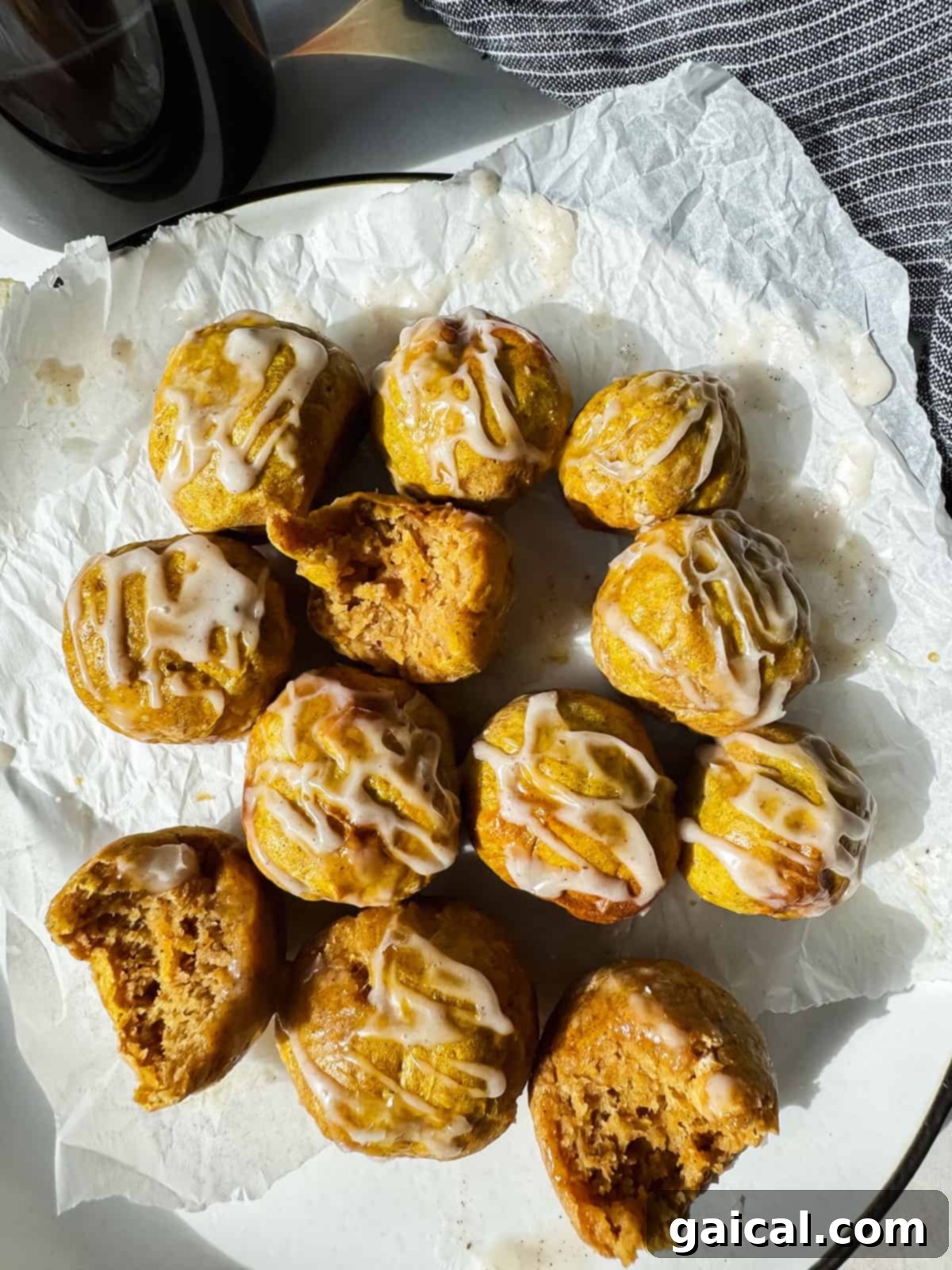 Spiced Pumpkin Air Fryer Bagel Treats 2 A plate of small, round pastries drizzled with white icing, some partially eaten, on a piece of parchment paper.