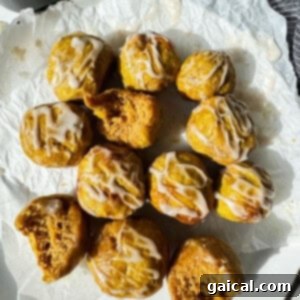 Spiced Pumpkin Air Fryer Bagel Treats 4 A dozen small, round cakes with white icing drizzle, some with bites taken out, are arranged on crumpled parchment paper under natural light.