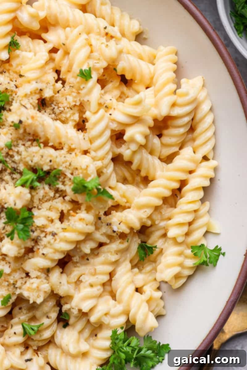 A close-up of a bowl of creamy pasta topped with golden breadcrumbs and garnished with fresh parsley.