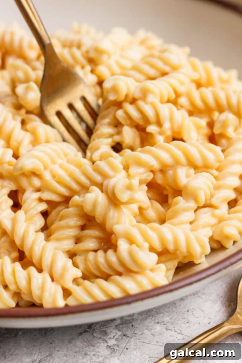 A fork twirls creamy cheese sauce-covered rotini pasta in a bowl on a textured surface.