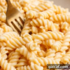 Close-up of a fork in a bowl of creamy, spiral macaroni and cheese.