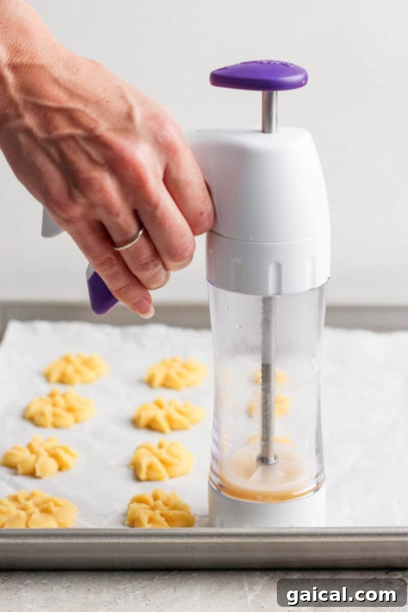 Mabel's Signature Spritz Cookies 4 A hand gently pressing buttery cookie dough into delicate flower shapes onto a parchment-lined baking sheet using a classic cookie press.