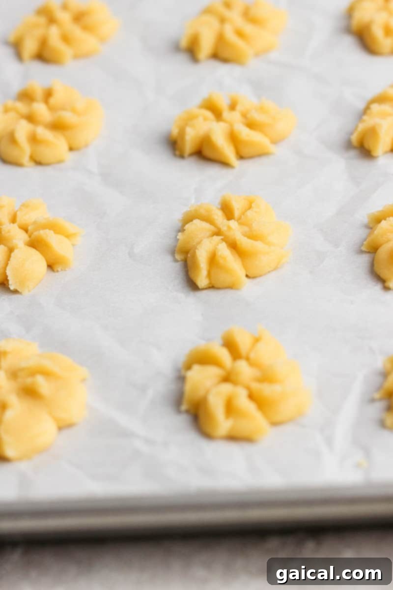 Mabel's Signature Spritz Cookies 5 A pristine baking sheet lined with parchment paper, showcasing rows of unbaked flower-shaped cookie dough, perfectly pressed and ready for the oven.
