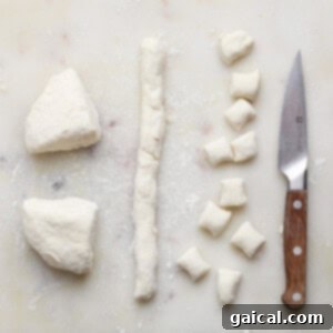 Dough is cut into small pieces on a white cutting board with a wooden-handled knife beside them.