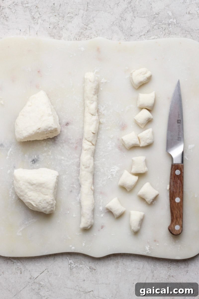 Pillowy Cottage Cheese Gnocchi 3 Dough being prepared on a cutting board with a knife. Dough is rolled into a log and cut into small pieces.