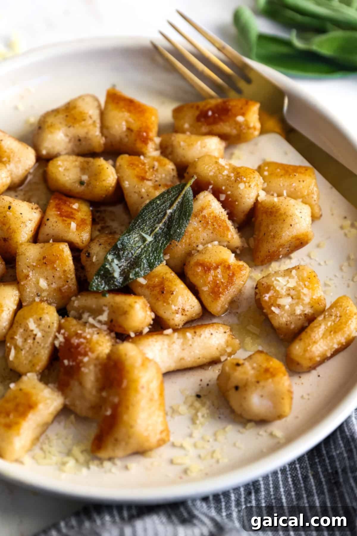 Pillowy Cottage Cheese Gnocchi 7 A plate of cottage cheese gnocchi topped with grated cheese and garnished with a sage leaf. A fork rests on the plate beside the gnocchi.