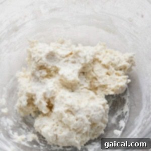 A clear bowl containing a mixture of flour and butter, forming a crumbly dough.